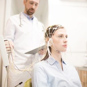 Woman hooked up to an EEG machine with sensors on her head with a doctor standing behind her